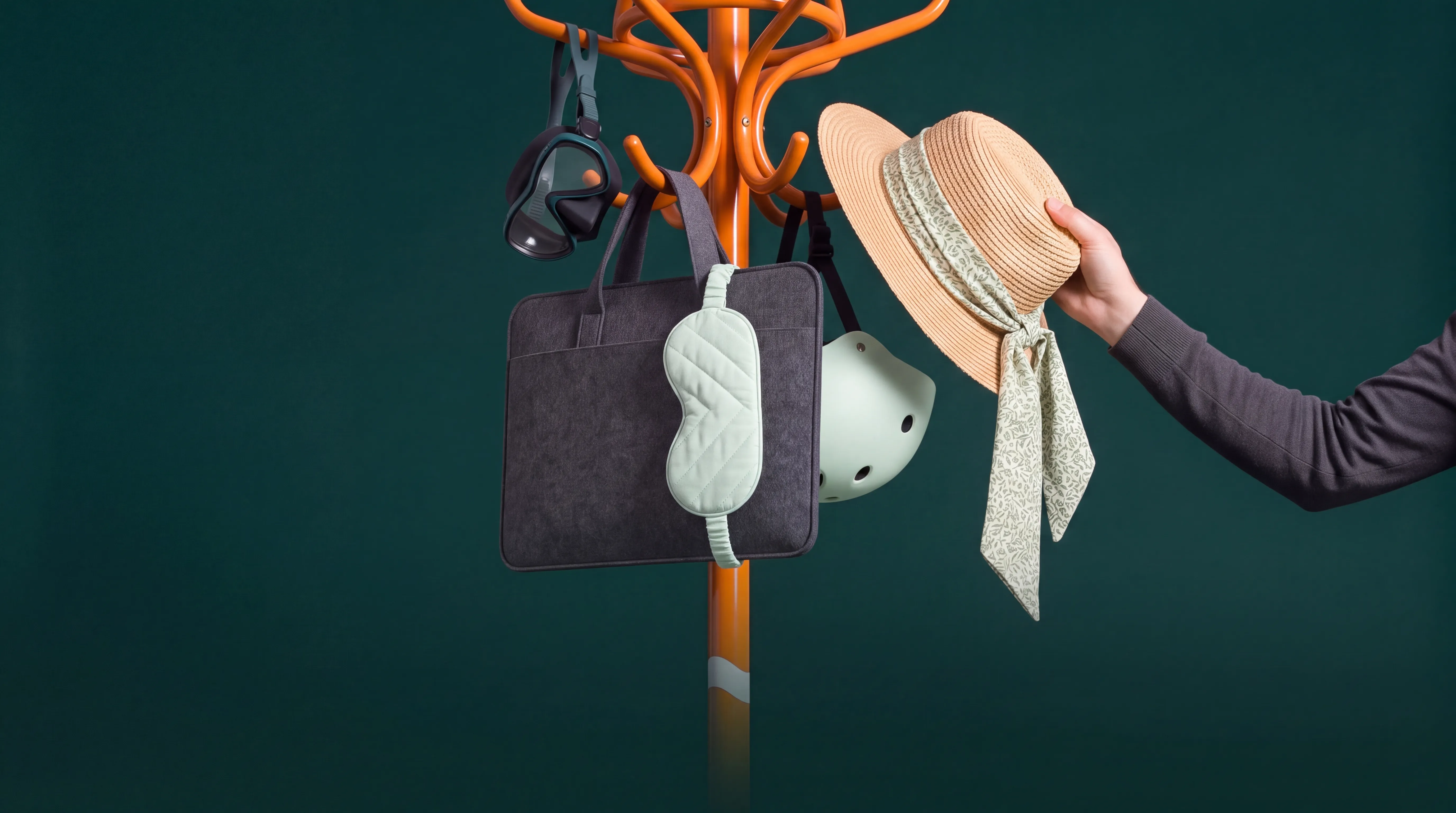 Portemanteau orange Monizze portant un masque de plongée, une sacoche d'ordinateur, un masque de sommeil, un casque de vélo et un chapeau de paille qu'une main décroche